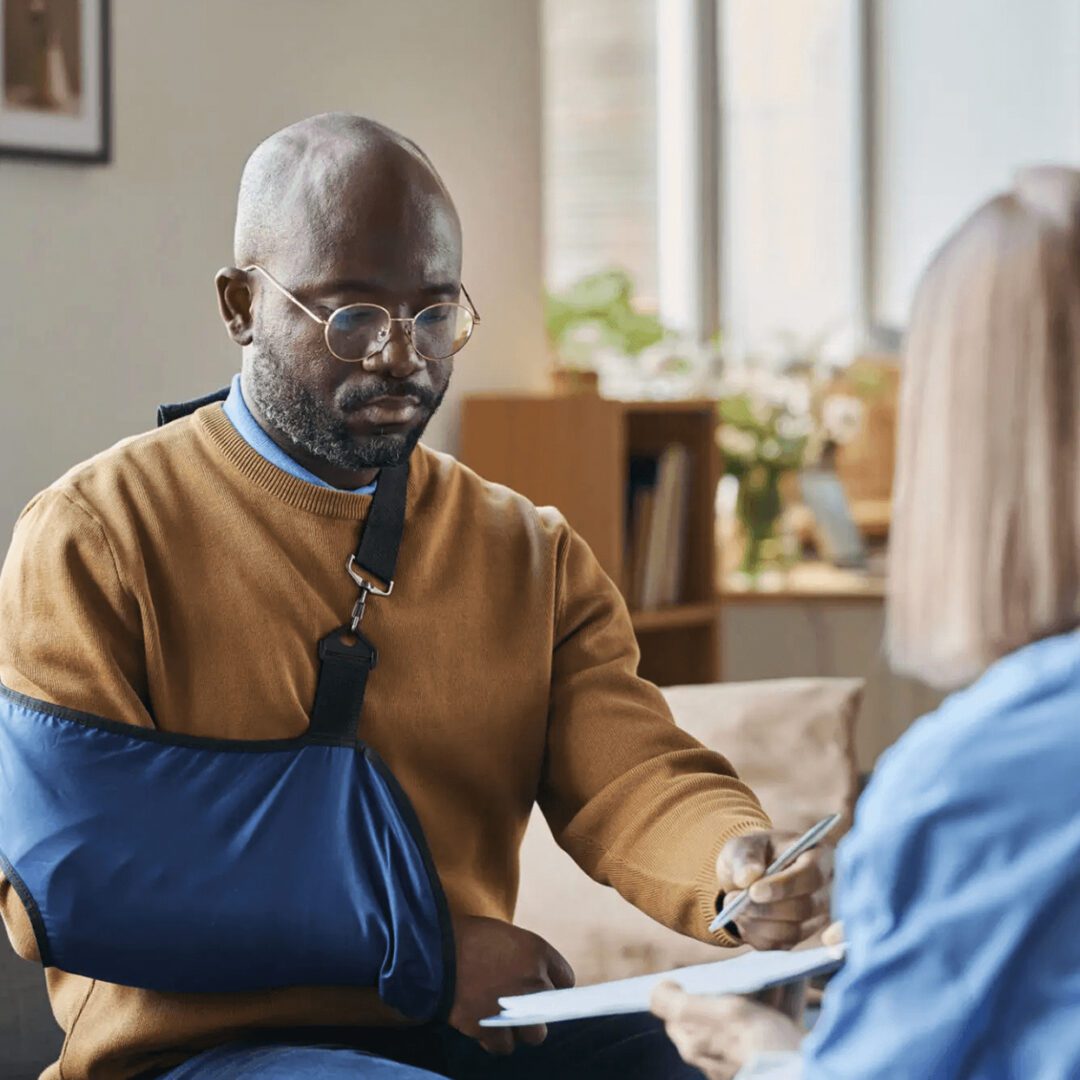 A man with a sling on his arm in a serious conversation with a healthcare professional.