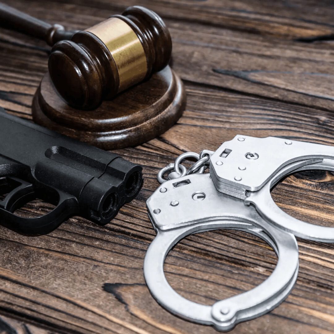A gun, handcuffs, and a judge's gavel on a wooden surface.