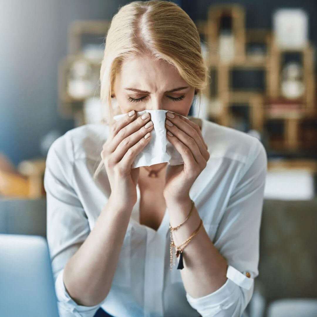 Woman blowing her nose with a tissue indoors.