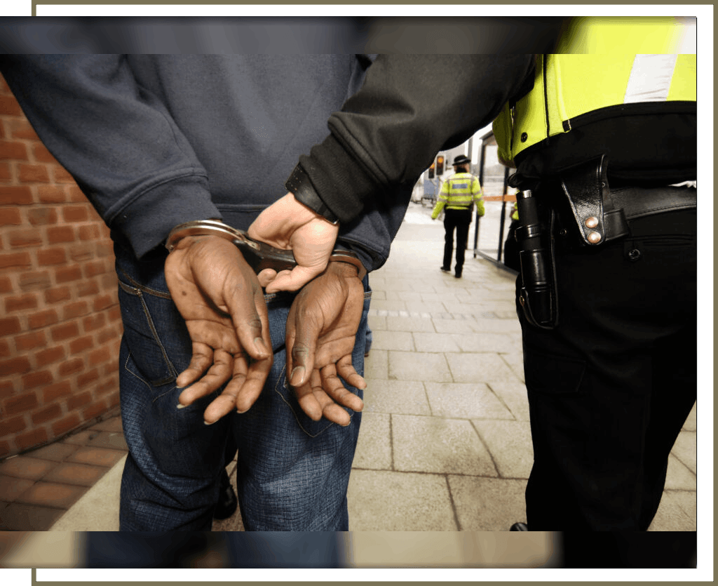 Person handcuffed by police officer on sidewalk.